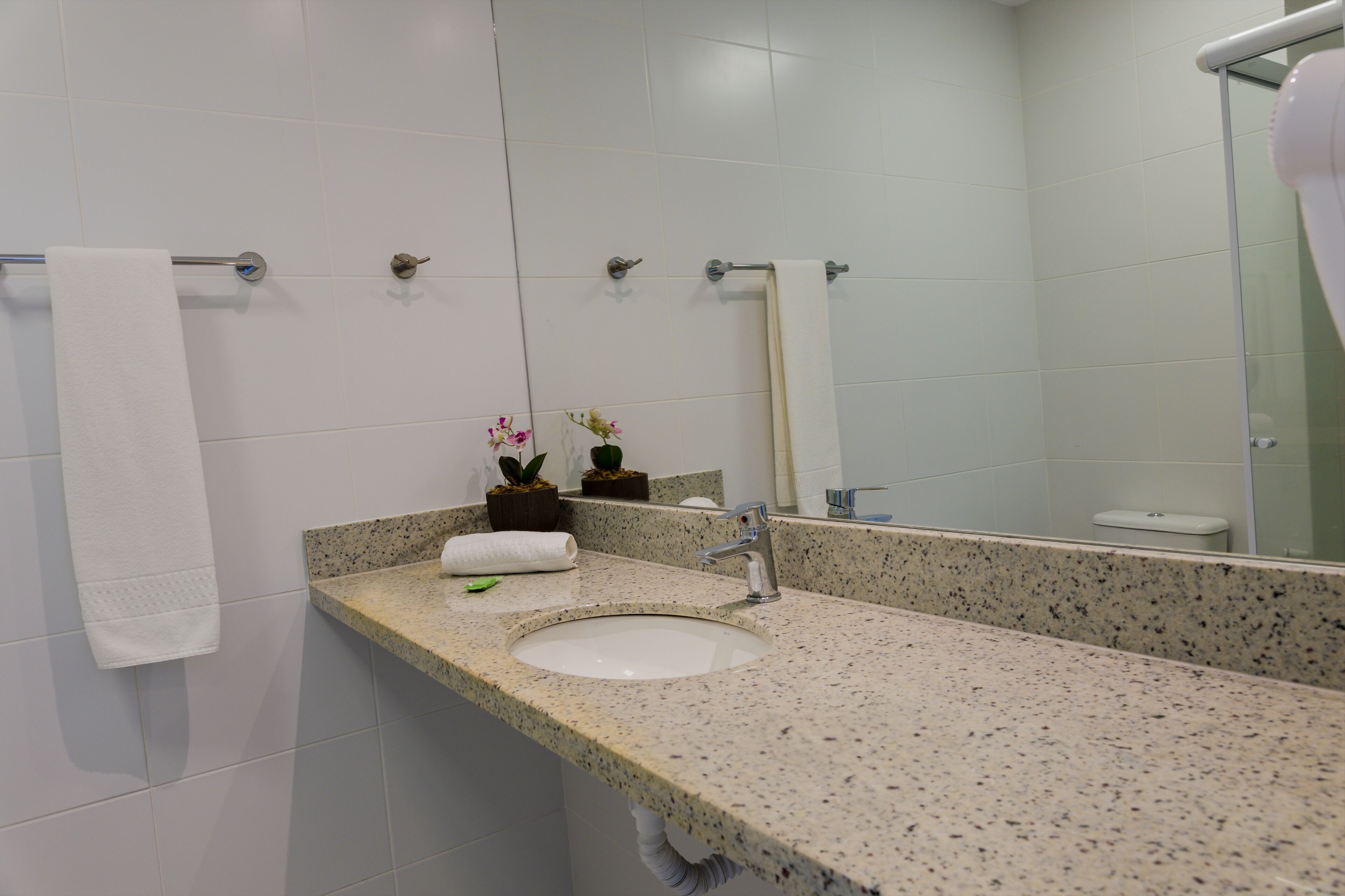 A bathroom with a granite countertop sink, a mirror, and a towel rack.