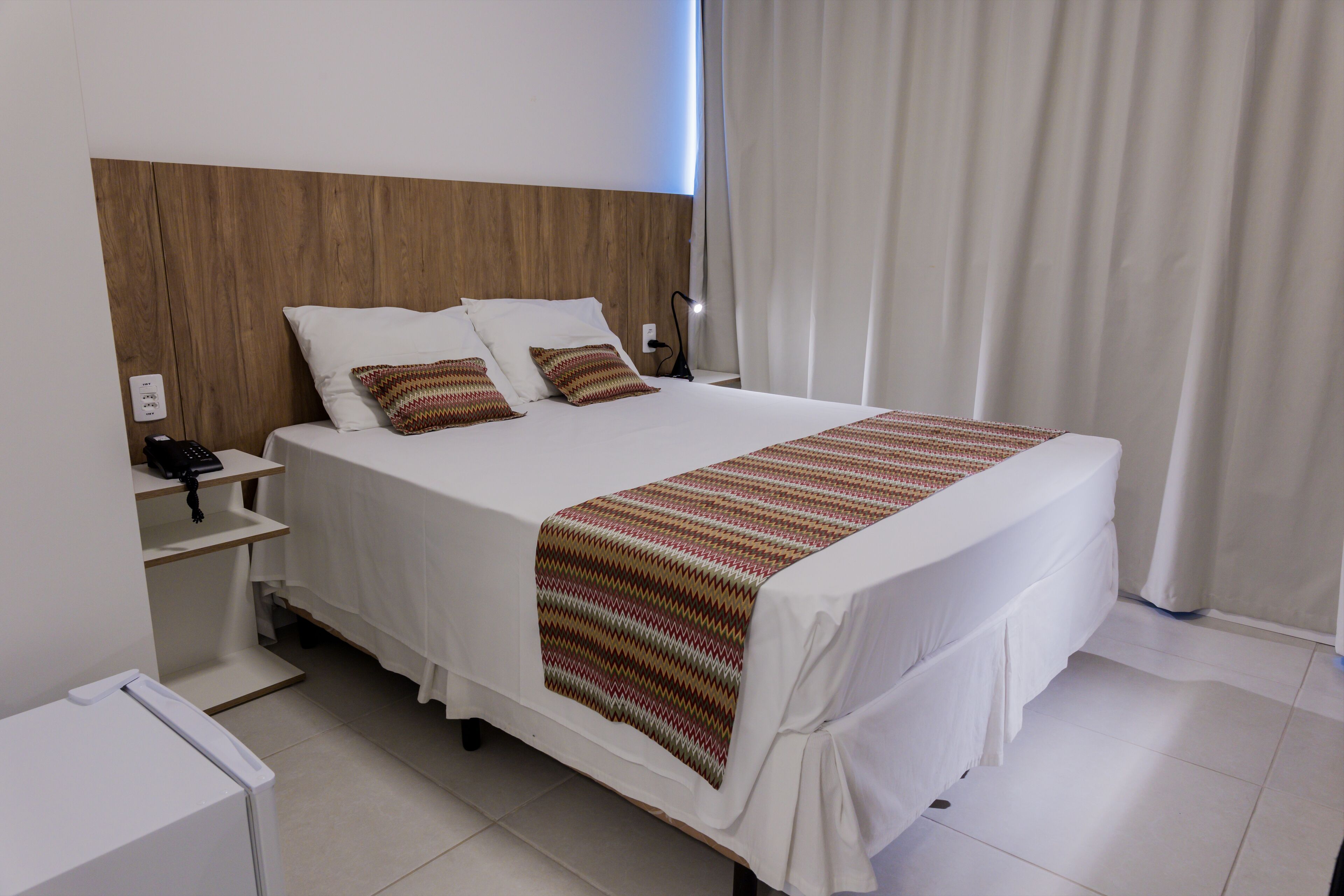 A neatly made bed with a striped blanket, a wooden headboard, and a bedside table with a phone.