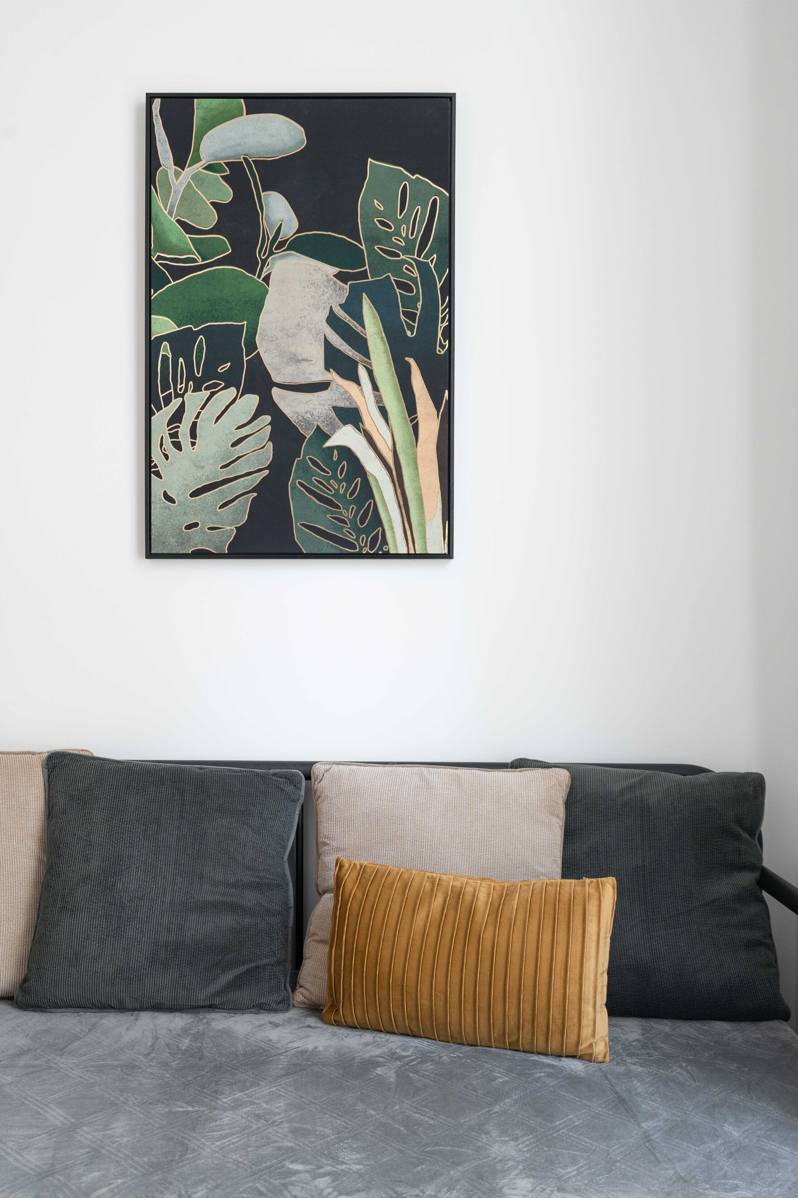 A framed botanical illustration on a wall above a grey sofa with two cushions.