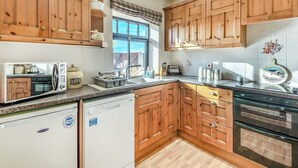 A modern kitchen with wooden cabinets, a built-in oven, a dishwasher, and a window with a view. - Betty Hutton - UK36661 (Belchford)