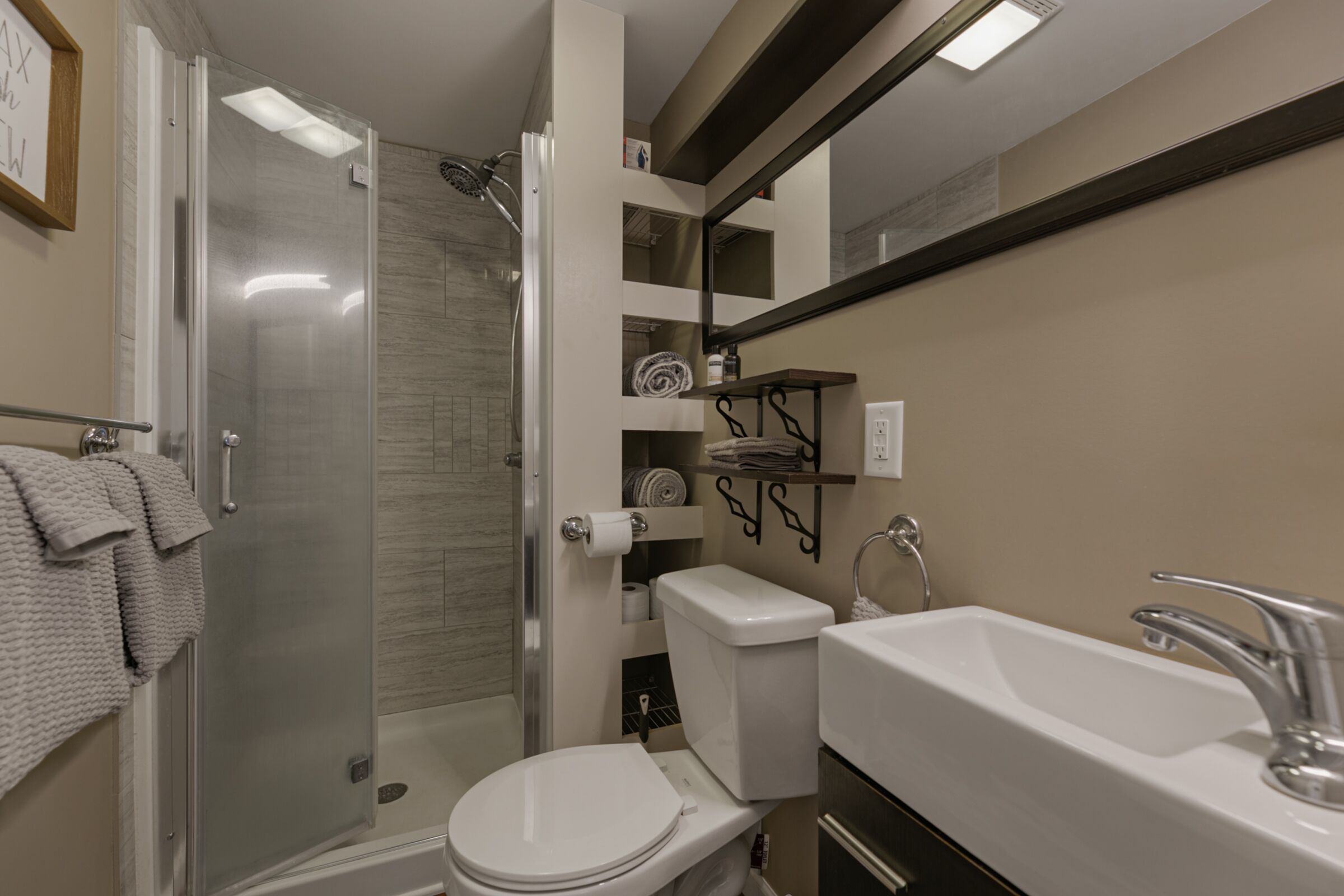 Et moderne badeværelse med en brusekabine i glas, et hvidt toilet og en vask med et spejl over.