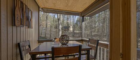A wooden deck with a table and chairs, a decorative vase, and a view of a forested area.