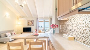 Eine moderne Küche mit Holzausstattung, ein Essbereich mit Tisch und Stühlen, ein Fernseher und ein Blick ins Freie.
