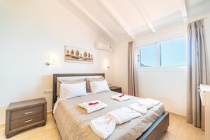 A neatly made bed with towels, a bedside table, a wall-mounted light, and a window with curtains.