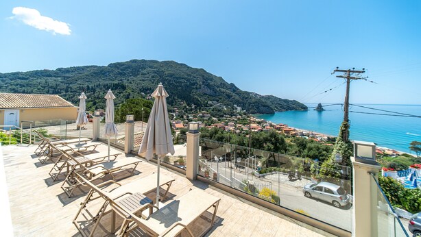 Eine Dachterrasse mit Liegestühlen und Sonnenschirmen mit Blick auf eine Küstenstadt und das Meer.