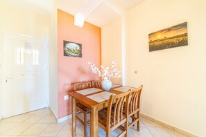 A dining area with a wooden table, chairs, a vase with flowers, and two paintings on the walls.