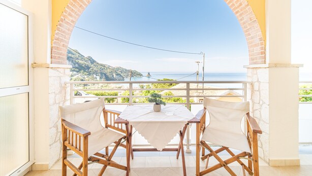 Een balkon met een tafel en stoelen, met uitzicht op de kust.