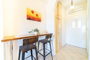 A kitchen with a wooden countertop, two bar stools, a potted plant, and a wall-mounted painting of hot air balloons. - Studio Apartment "Mazis Studio A" with Sea View, Balcony & Wi-Fi (Corfu)