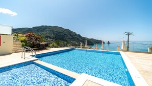 Ein rechteckiger Swimmingpool mit blauen Mosaikfliesen, einer Holzterrasse und Blick auf eine Berglandschaft.