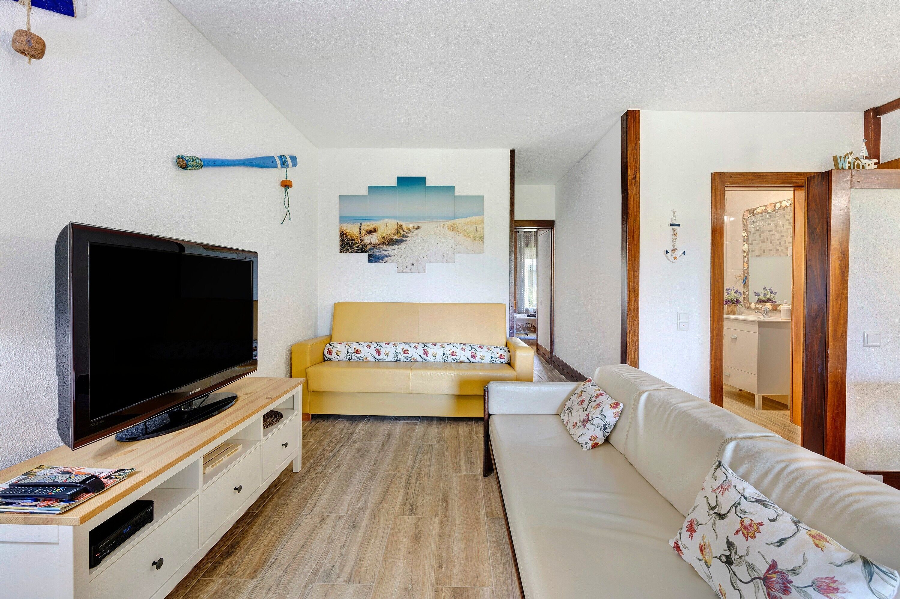Un salon moderne avec un téléviseur à écran plat, un canapé jaune, un canapé blanc et un meuble de rangement en bois.