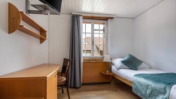 A bedroom with a bed, a desk, a chair, a TV mounted on the wall, and a window with curtains.