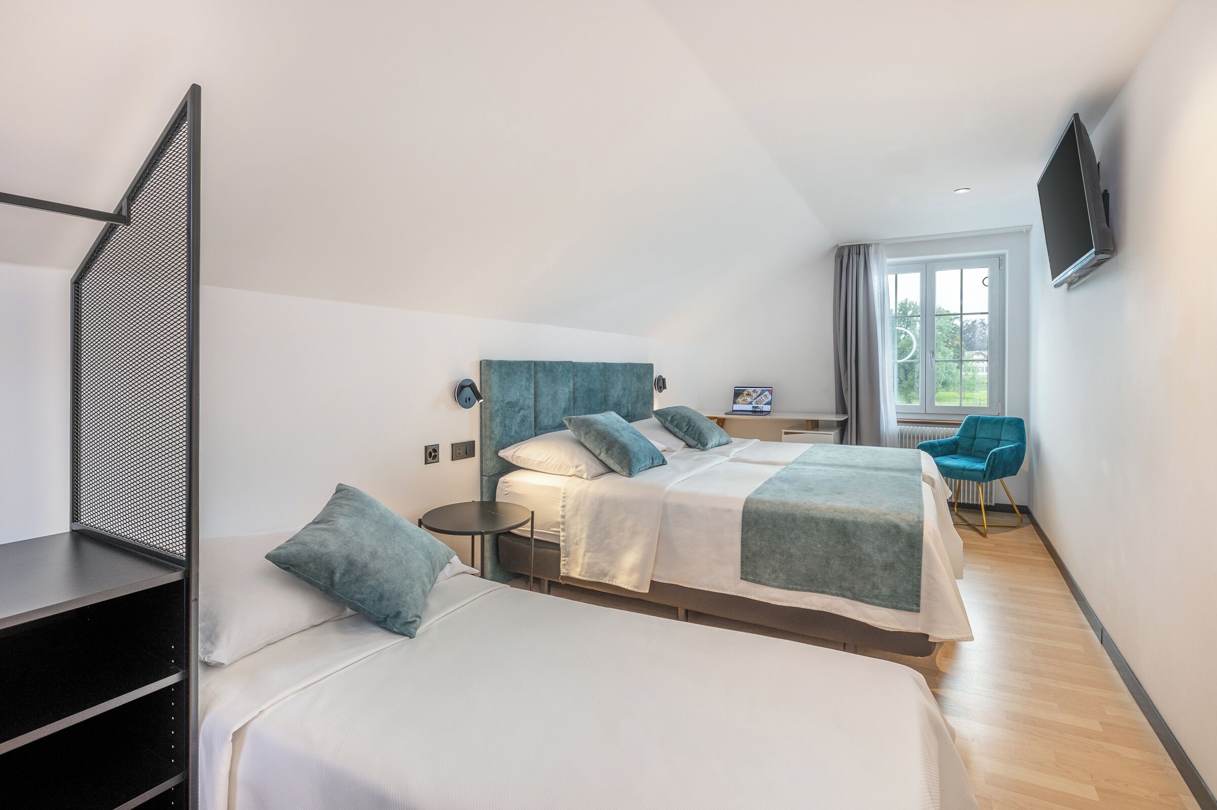 A modern hotel room with two beds, a desk, a chair, and a TV.
