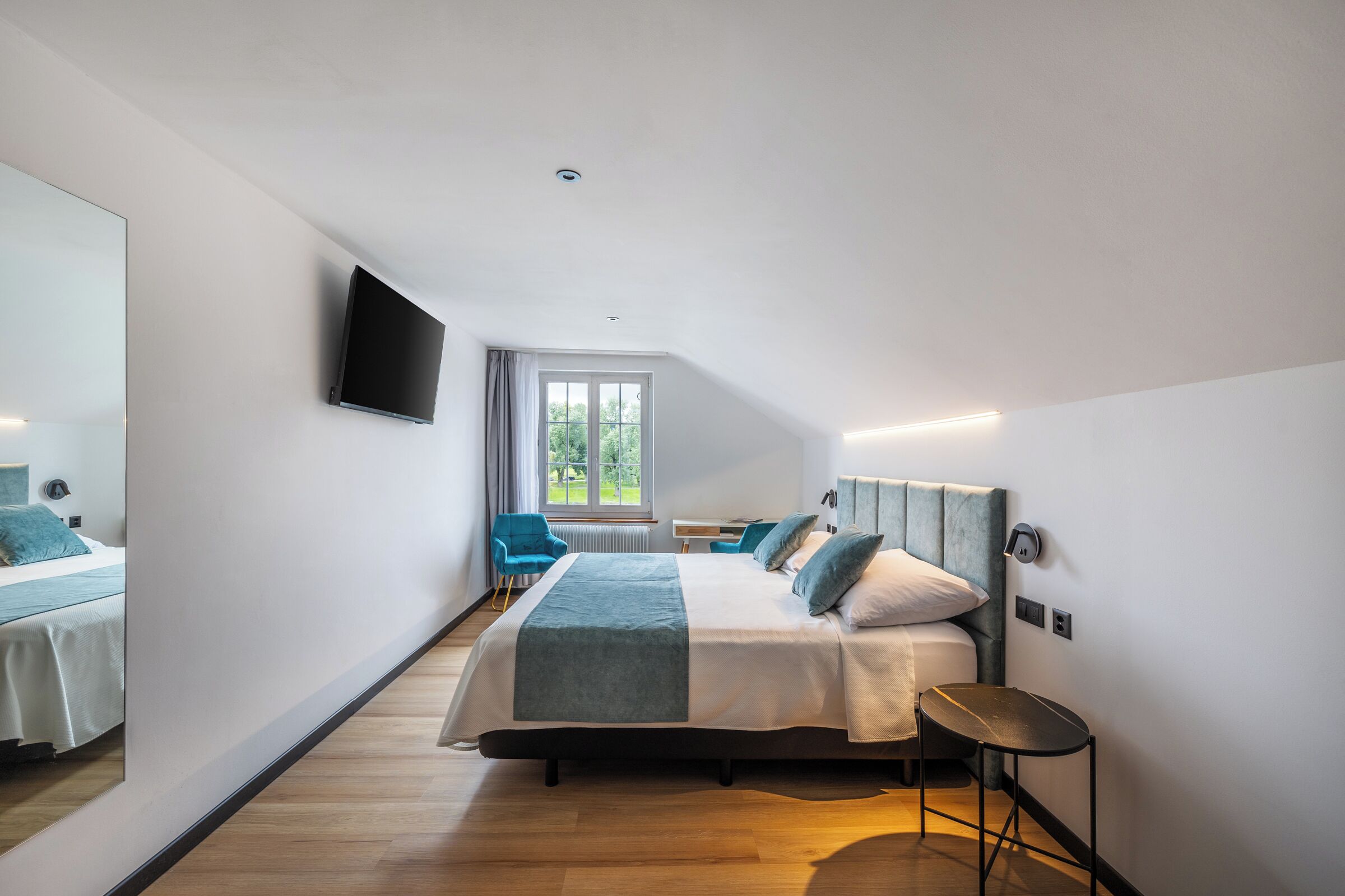 A modern hotel room with a large bed, a desk, a chair, and a TV mounted on the wall.