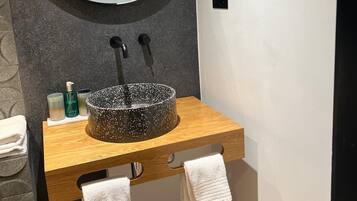 A bathroom with a round mirror, a black speckled sink, and two towels hanging from a wooden cabinet.