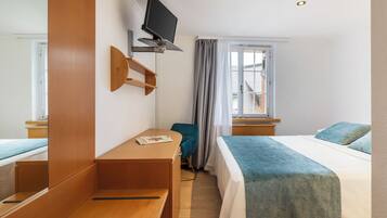 Una habitación de hotel con cama, escritorio, silla, televisión y ventana con cortinas.