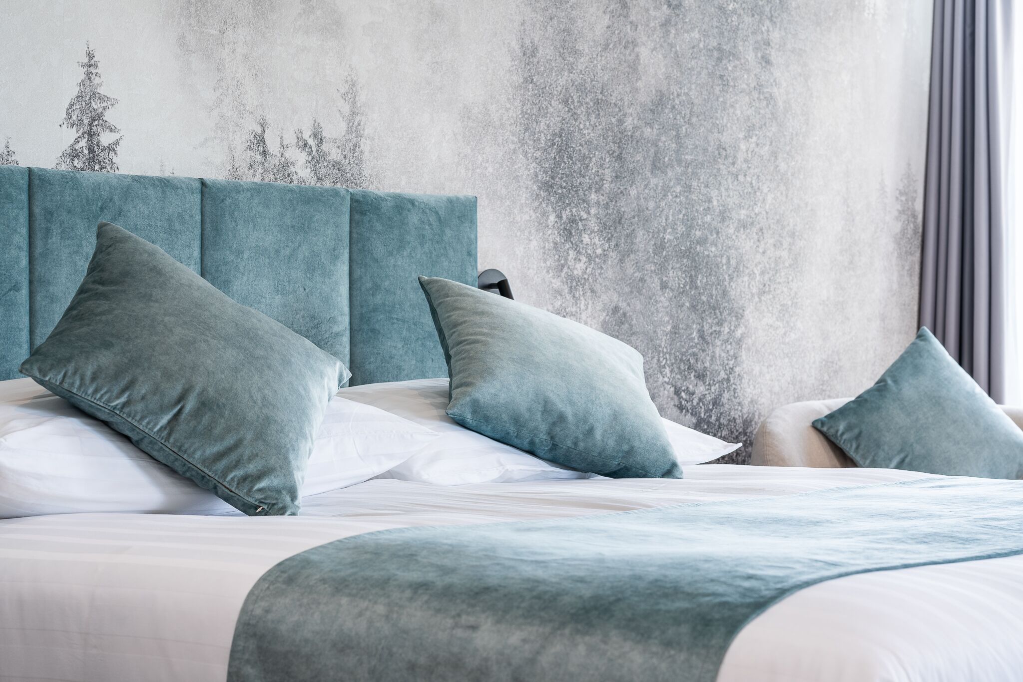 Una cama cuidadosamente tendida con un cabecero color aguamarina y almohadas a juego, frente a una pared con textura.