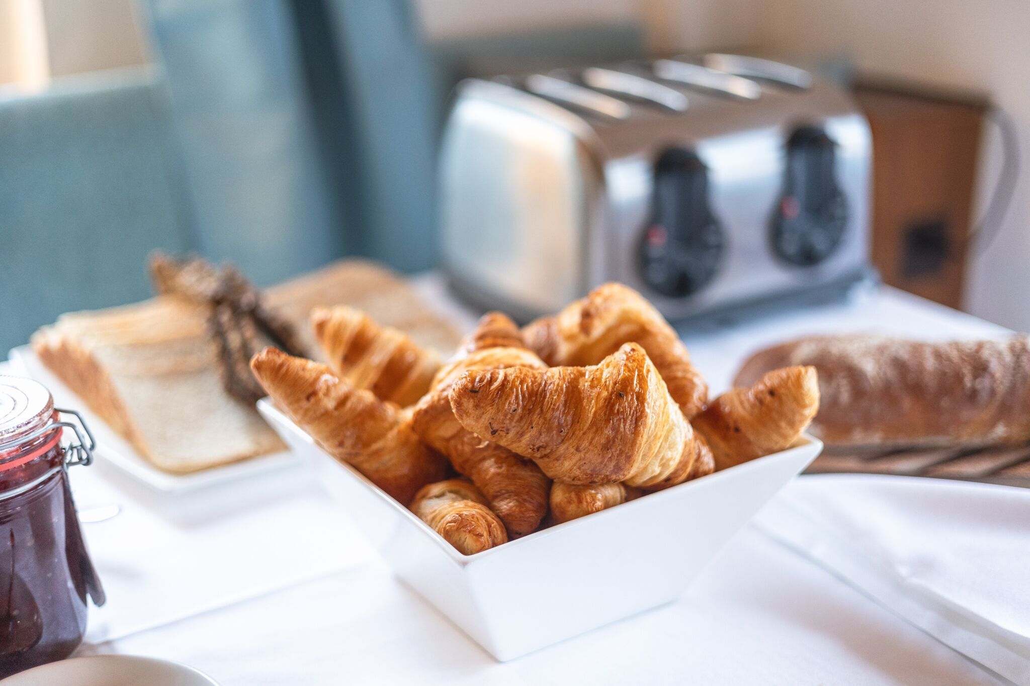 A breakfast setting with croissants, a jar of jam, and a toaster.