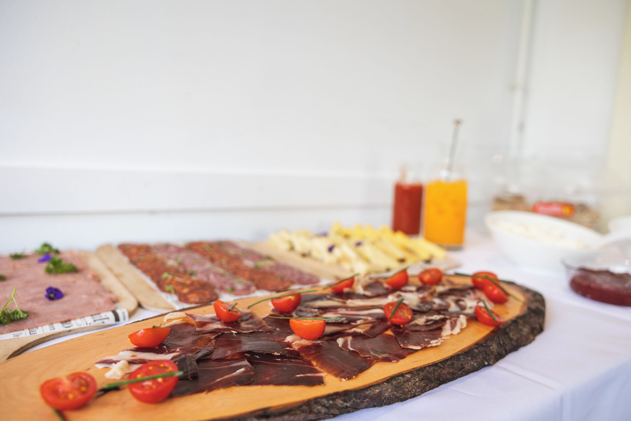 Une variété d’aliments, notamment des viandes, des fromages et des fruits, disposés sur une planche en bois, avec une bouteille de ketchup et un verre de jus d’orange en arrière-plan.