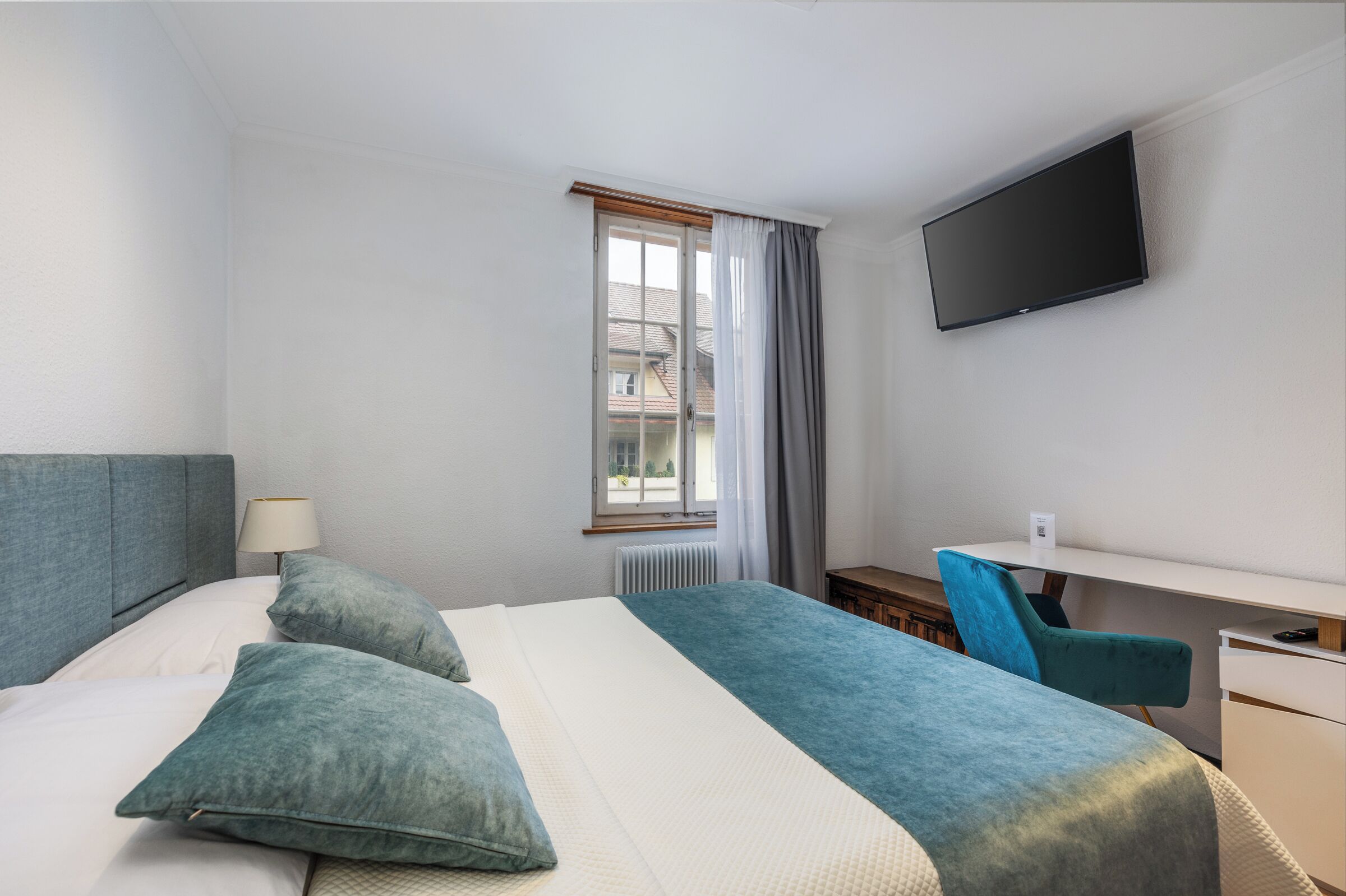 Une chambre d’hôtel avec un lit, un bureau, une chaise, une télévision et une fenêtre avec des rideaux.