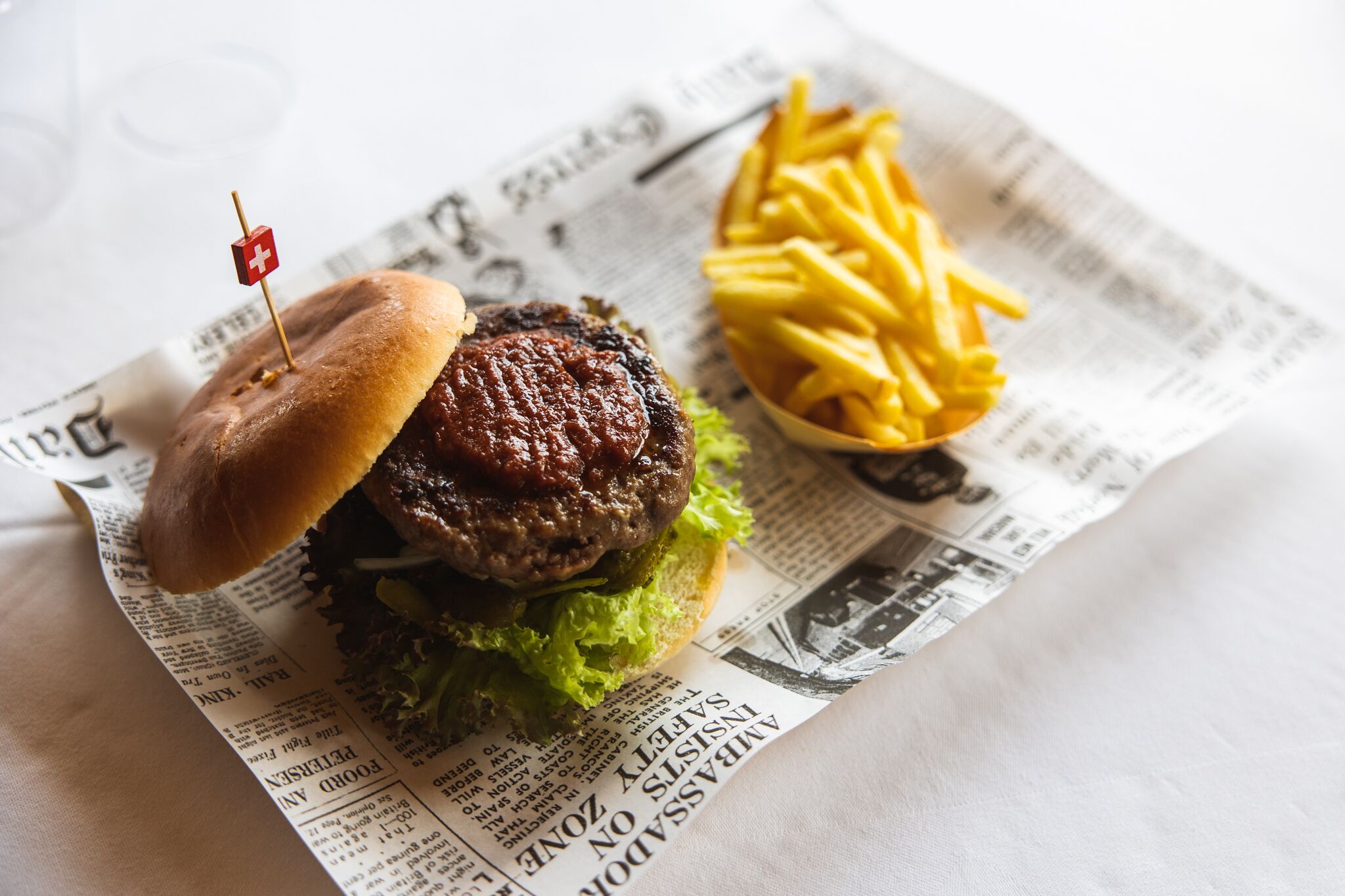 Un hamburger servi dans un pain, avec de la laitue et un petit drapeau planté sur le dessus, le tout présenté sur un journal.