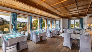 Un comedor amplio con varias mesas dispuestas para una comida, ventanas grandes con cortinas y vistas al exterior.