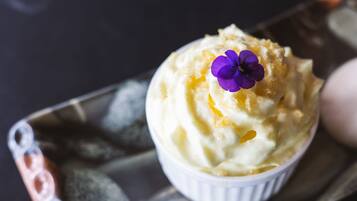 A dessert in a white ramekin on a tray with a purple flower on top.