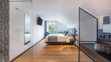 Un dormitorio moderno con cama, televisor, ventana grande y baño con lavamanos y espejo.