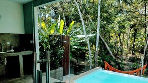 A glass-enclosed pool area with a chair and a table, surrounded by lush greenery and a hammock. - Cabin in Arraial d'Ajuda with Private Pool (Arraial d'Ajuda)