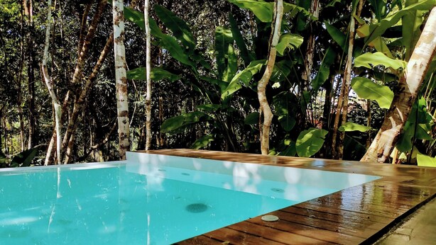 A rectangular pool with a wooden deck, surrounded by dense foliage. - Cabin in Arraial d'Ajuda with Private Pool (Arraial d'Ajuda)