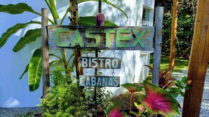 A wooden sign with "CASTEX" and "BISTRO CABANAS" written on it, surrounded by lush greenery and plants. - Cabin in Arraial d'Ajuda with Private Pool (Arraial d'Ajuda)