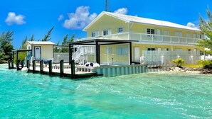 A beachfront property with a large yellow building, a dock extending into turquoise waters, and a clear blue sky. - Bimini Vacation Apartment - Apt #4 (Bimini)
