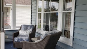 A covered porch with two wicker chairs and a small table, large windows with white frames, and a blue exterior wall. - Charming unique historical home on Main street, in the heart of Downtown Bozeman (Bozeman)