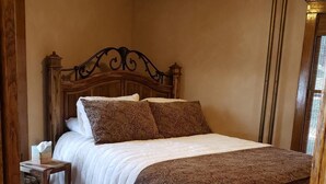 A wooden four-poster bed with a white and brown patterned bedspread, a bedside table with a tissue box, and a wooden floor. - Charming unique historical home on Main street, in the heart of Downtown Bozeman (Bozeman)