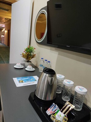 A hotel room with a TV mounted on the wall, a small potted plant, a coffee maker, and a tray with water bottles and coffee packets. - Marblue Hotel (Mardin)