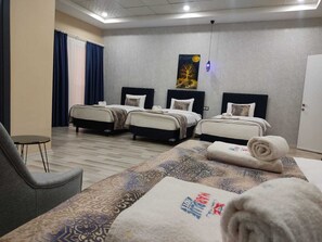 A hotel room with two beds, a small table, a chair, and a large bedspread with text. - Marblue Hotel (Mardin)