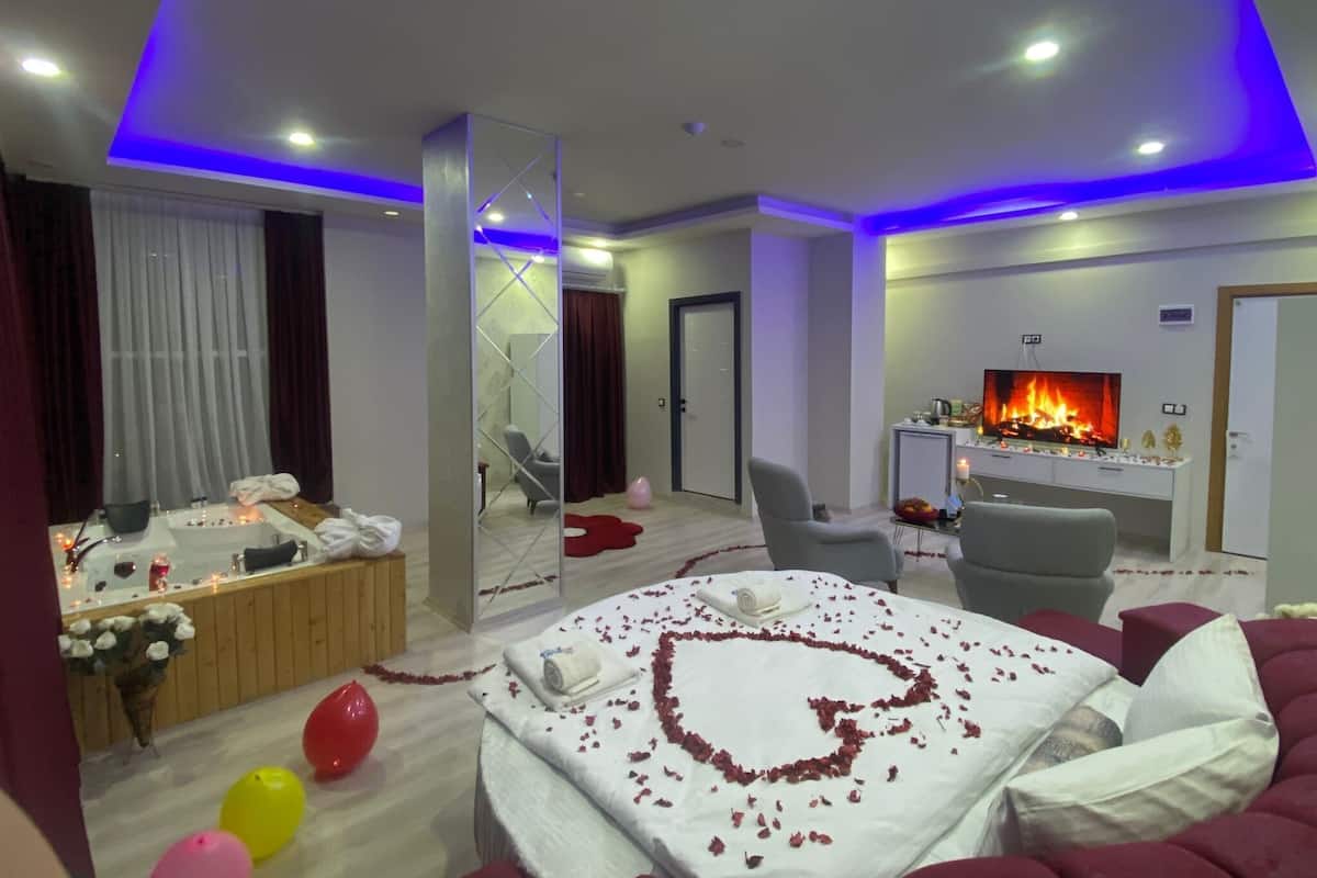 A hotel room with a bed, a TV, a fireplace, a mirror, and a seating area.