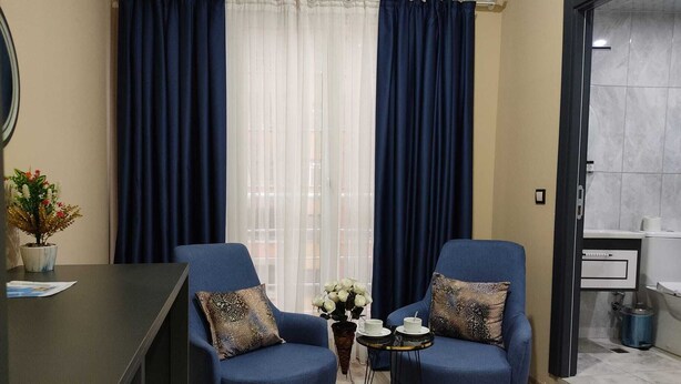 A room with two blue armchairs, a small table with cups, a potted plant, and a view through a window with blue curtains. - Marblue Hotel (Mardin)
