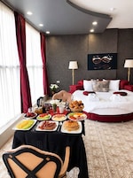 Habitación de hotel con una mesa de comedor dispuesta para el desayuno, una cama con ropa de cama roja y una obra de arte colgada en la pared.