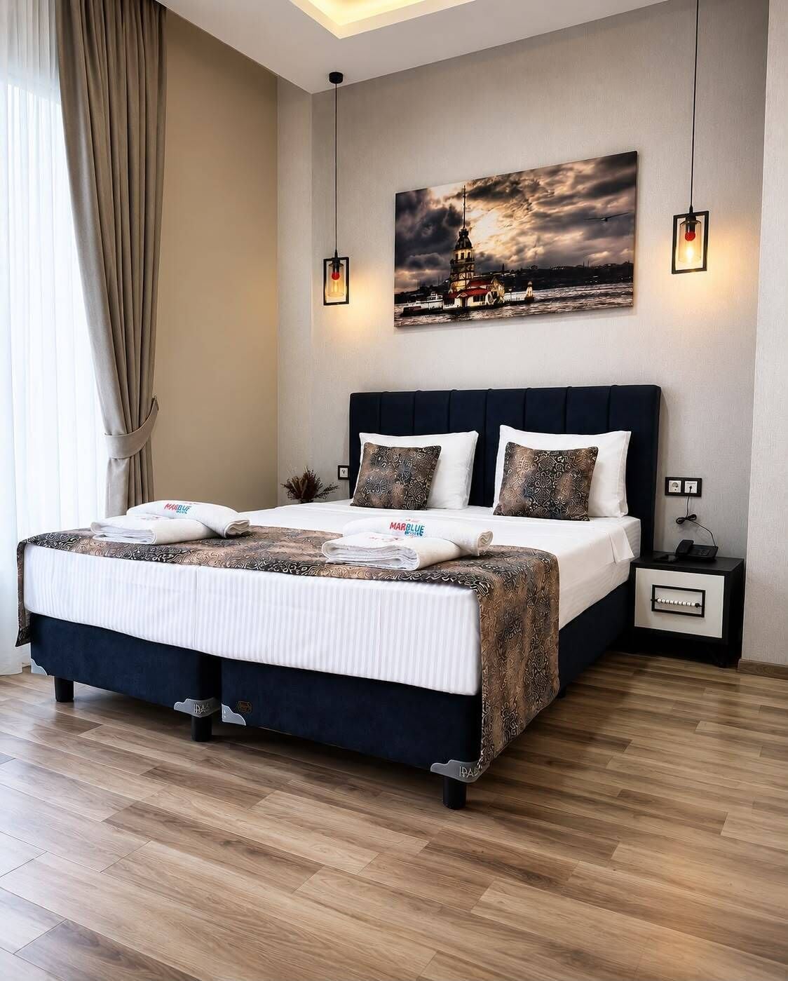 Habitación de hotel moderna con una cama grande, una mesita de noche, una lámpara de pared y un cuadro de un paisaje urbano.