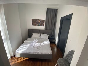 Una cama bien hecha con una toalla decorativa, un cabecero gris y un cuadro en la pared.