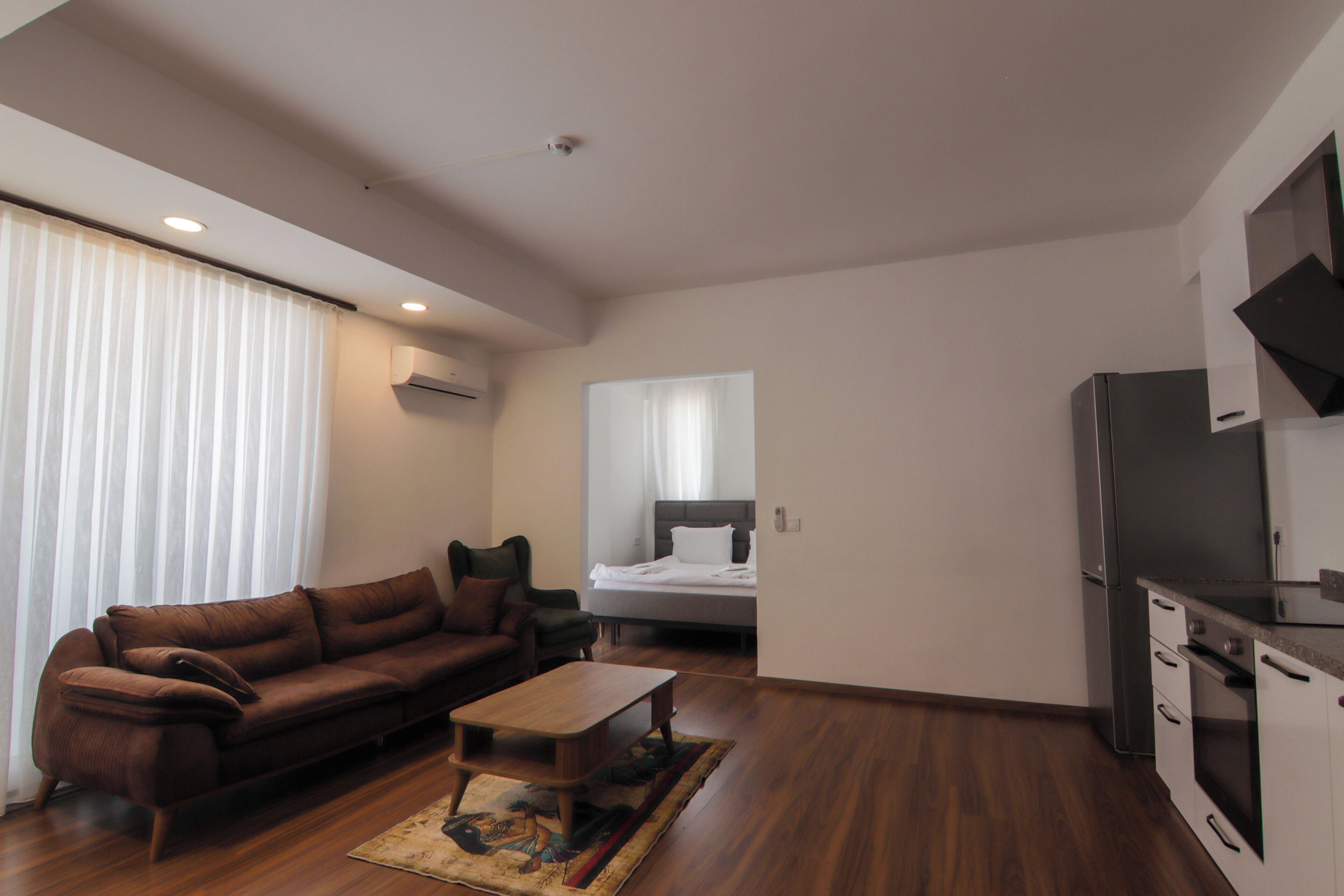 A modern living room with a sofa, a coffee table, and a bed in the background.