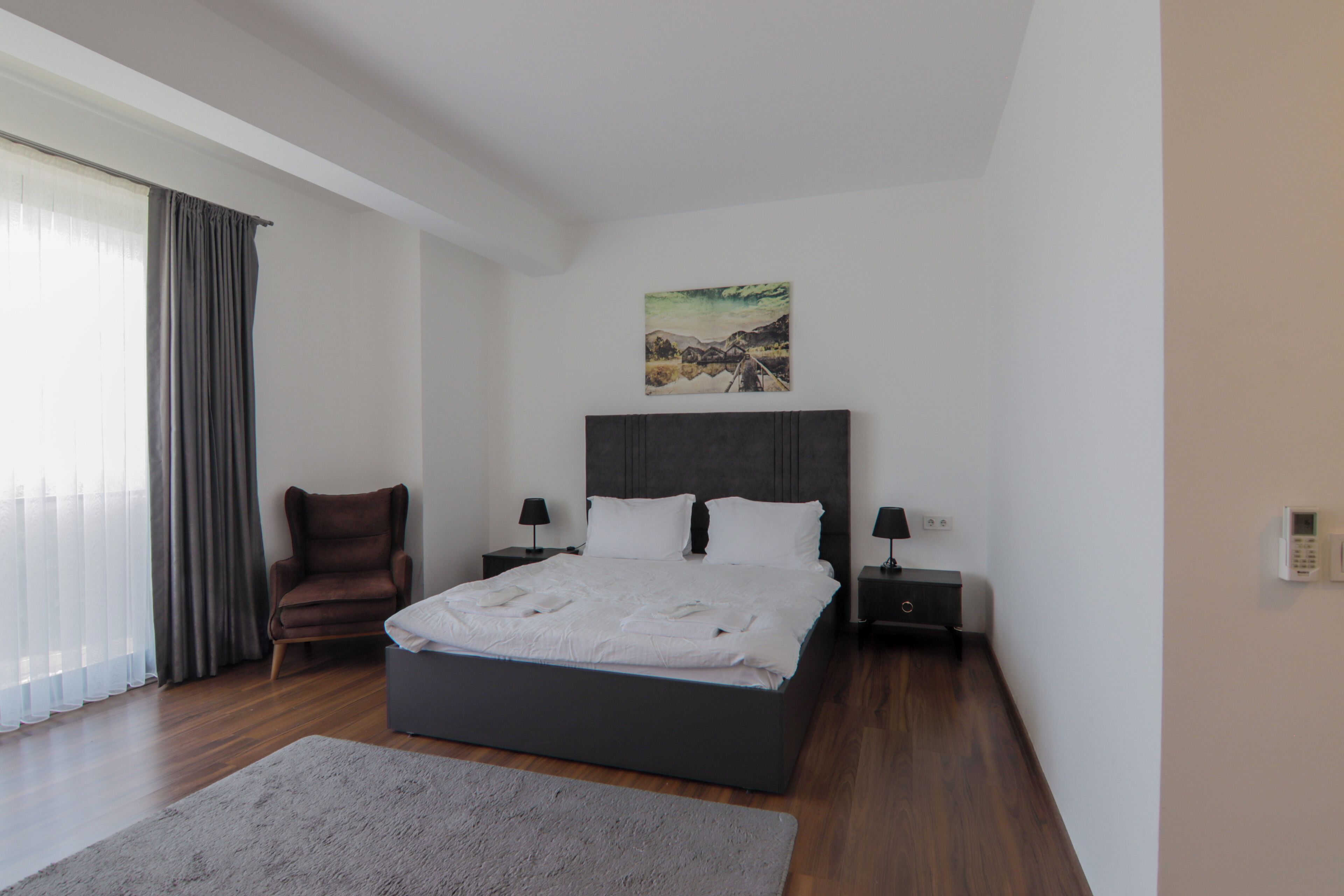 Un dormitorio moderno con una cama grande, una silla, una mesita de noche, una lámpara y un cuadro en la pared.