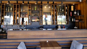 A bar area with wooden shelves displaying various liquor bottles, a seating area with benches, and a counter with a cash register. - Side Mira Palace (Manavgat)