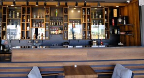 A bar area with wooden shelves displaying various liquor bottles, a seating area with benches, and a counter with a cash register. - Side Mira Palace (Manavgat)