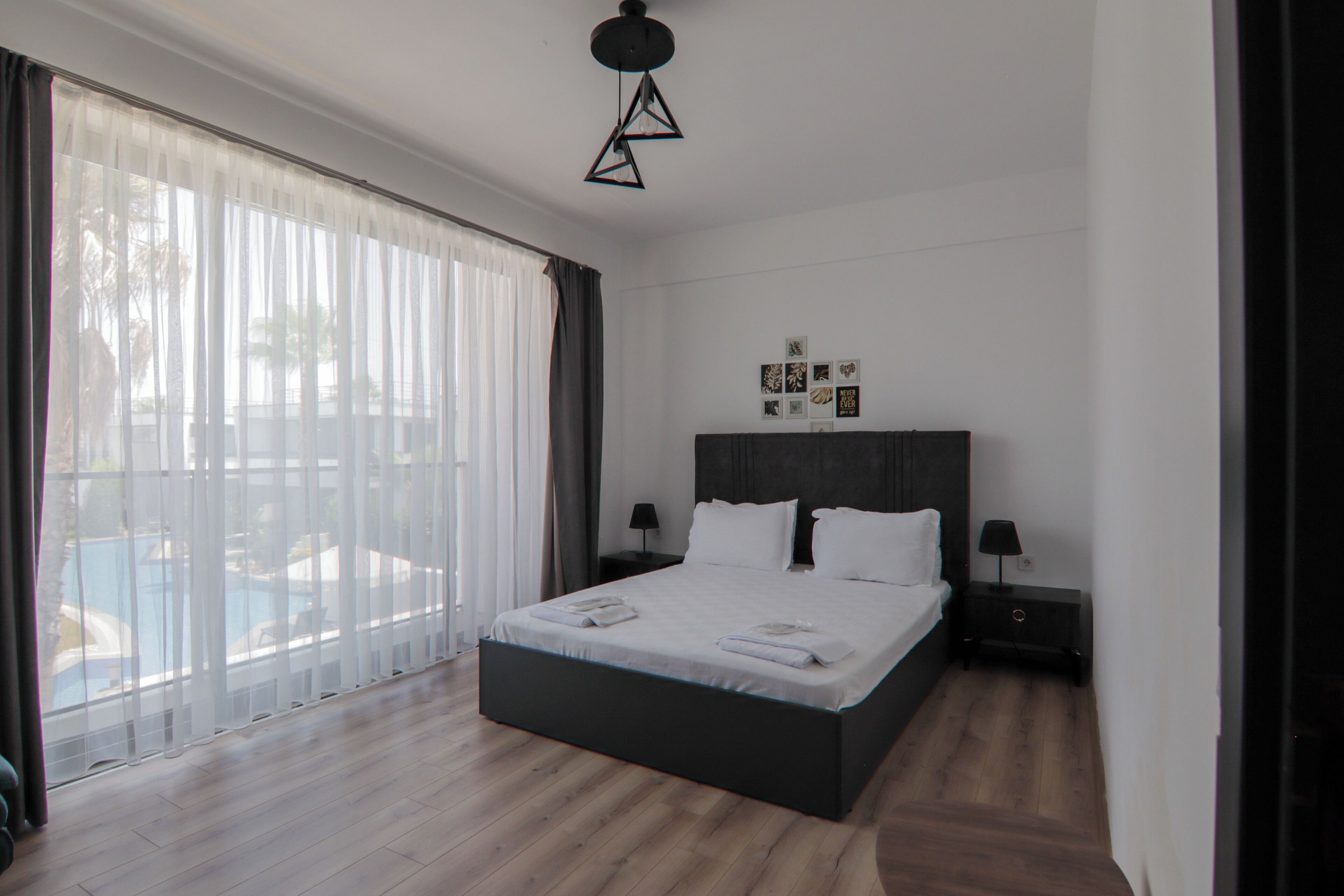 Una habitación de hotel moderna con una cama grande, vista a una piscina y una lámpara en el techo.