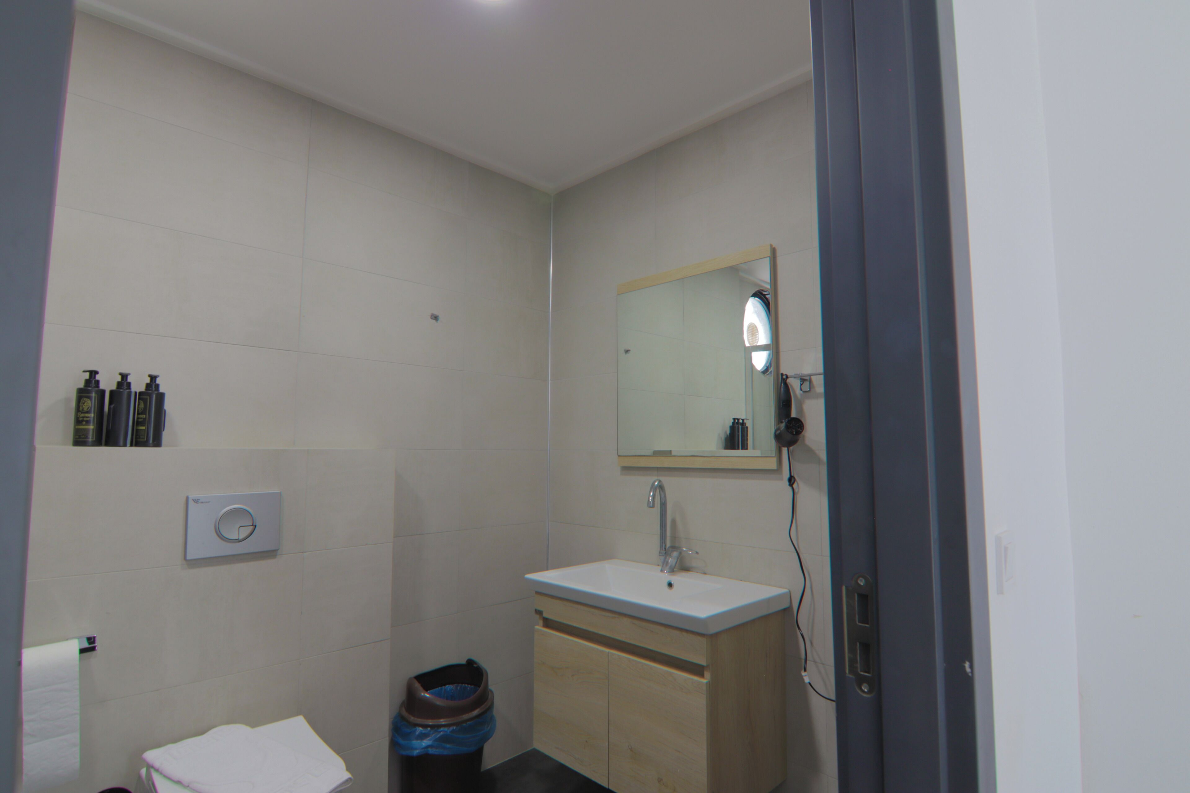 A small bathroom with a toilet, sink, mirror, and a trash bin.