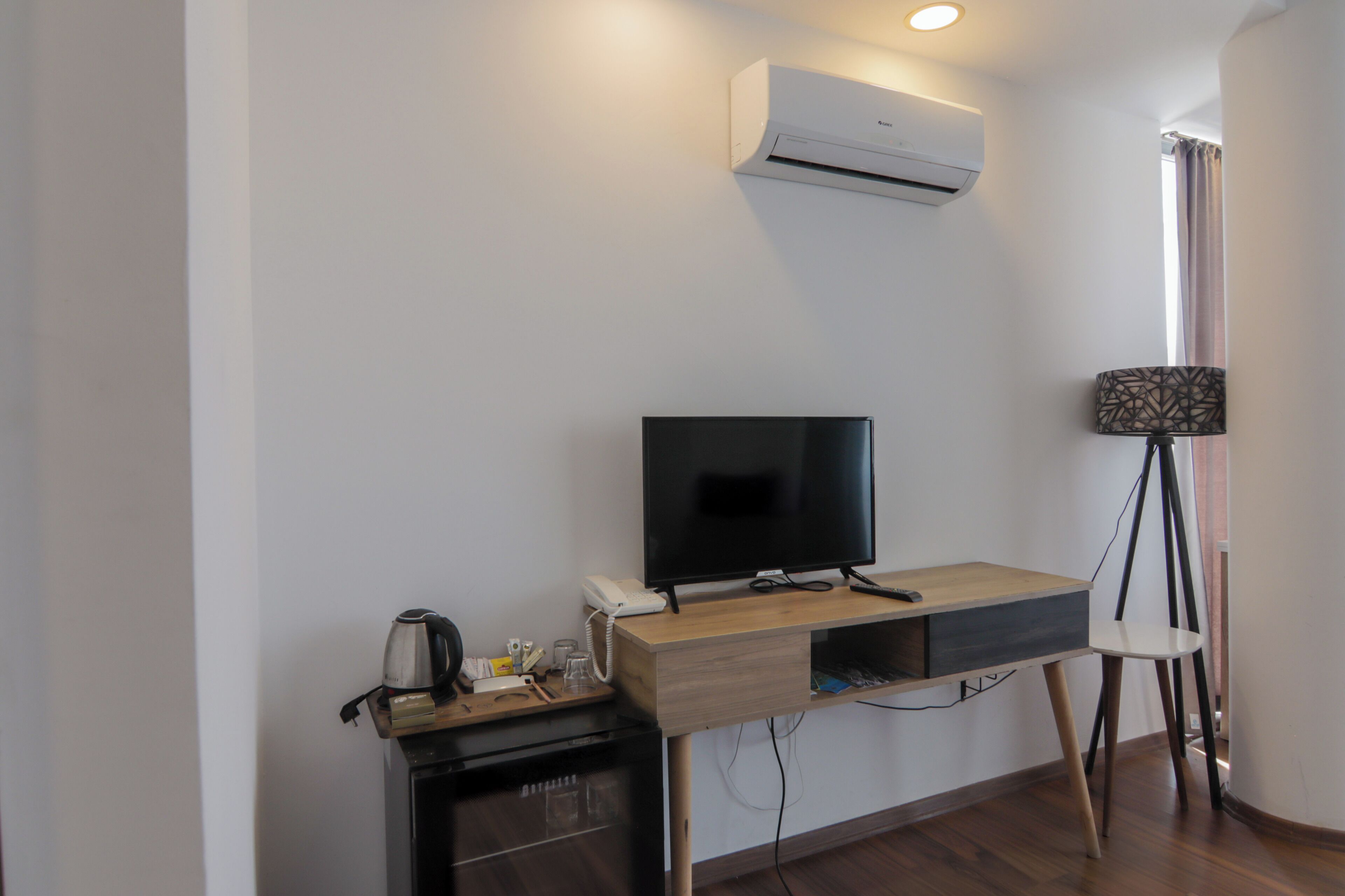 A modern room with a desk, television, air conditioning unit, and a lamp.