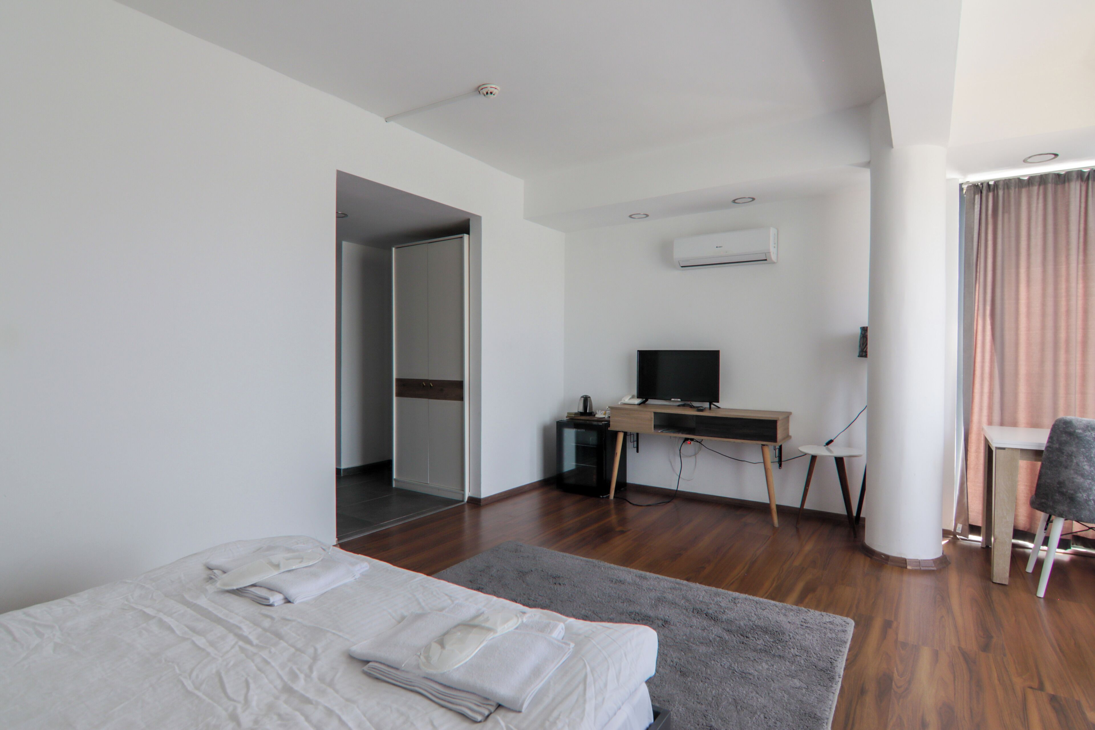 A modern hotel room with a bed, a desk, a television, and an air conditioning unit.