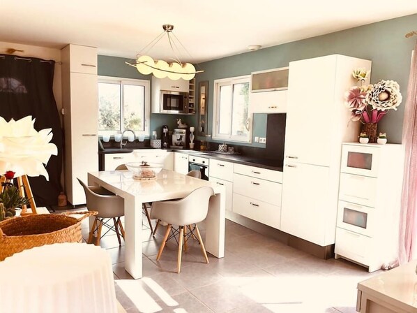 Une cuisine moderne avec des meubles blancs, un îlot central et un coin repas avec des chaises.