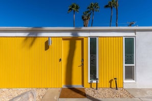 Um edifício amarelo com porta branca, janela e um pequeno degrau que dá acesso à entrada.